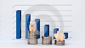 Business concept with miniature. TwoÃÂ smallÃÂ pinkÃÂ piggyÃÂ bankÃÂ onÃÂ theÃÂ stackÃÂ ofÃÂ coinsÃÂ inÃÂ frontÃÂ ofÃÂ theÃÂ graph.